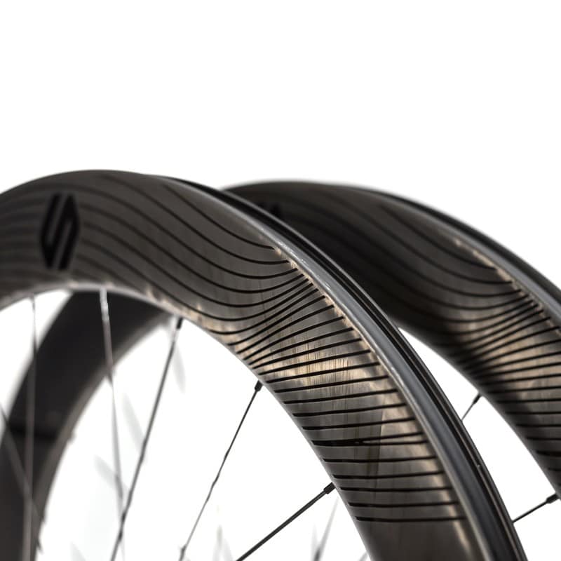 Primer plano de unas llantas tubeless Speedsix México fabricadas en carbono, con un diseño aerodinámico y acabados en fibra de carbono expuesta con líneas onduladas. 