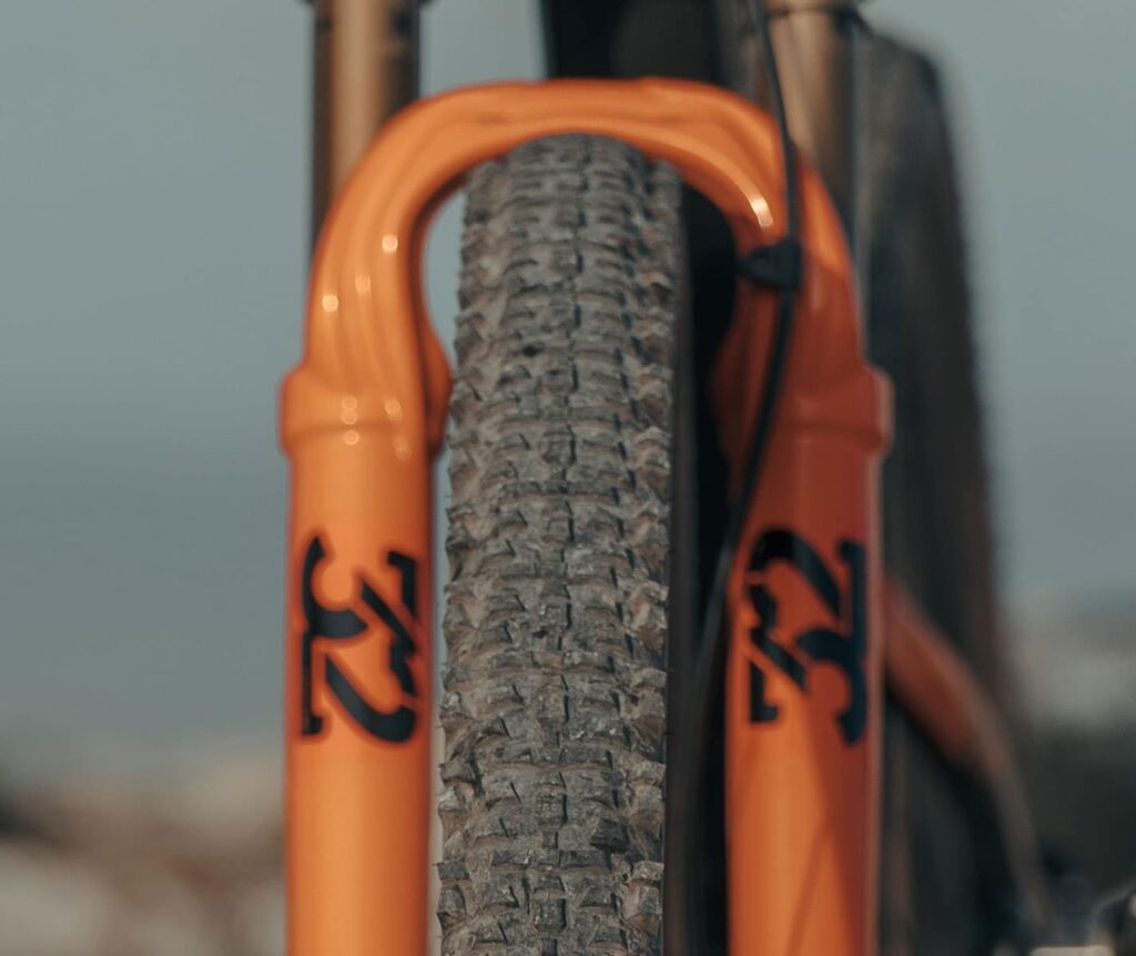 Primer plano de una llanta tubeless Speedsix México montada en una bicicleta de montaña con suspensión delantera de color naranja. La llanta tiene un diseño de taqueado agresivo, ideal para terrenos irregulares y técnicos.